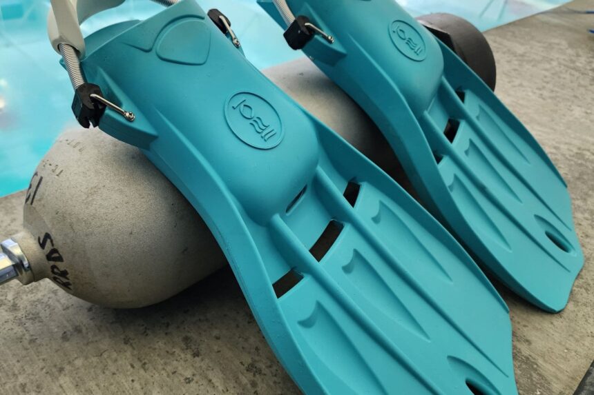 Fourth Element Tech fins in aqua resting on a scuba cylinder beside the pool