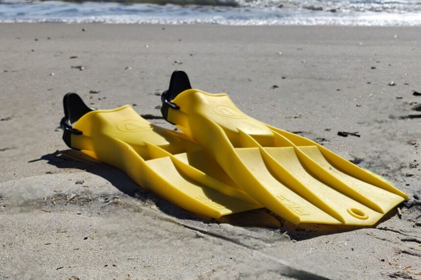 Pair of yellow Apeks RK3 fins lying on wet beach sand near the waterline