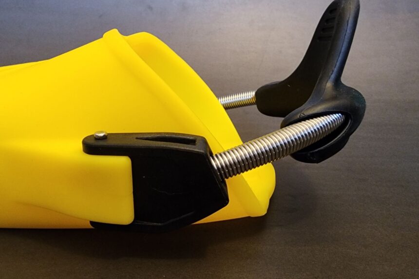 Close-up of the black pull tab and stainless spring strap on a yellow Apeks RK3 fin
