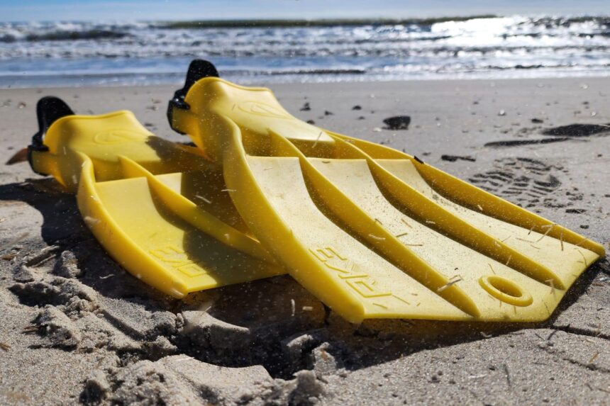 Yellow Apeks RK3 fins lying in dry sand with the surf breaking behind