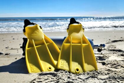 Yellow Apeks RK3 rubber fins propped against a scuba cylinder on the beach during testing
