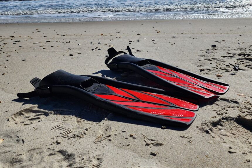 Pair of Atomic Aquatics SplitFins lying flat on the sand with the surf behind