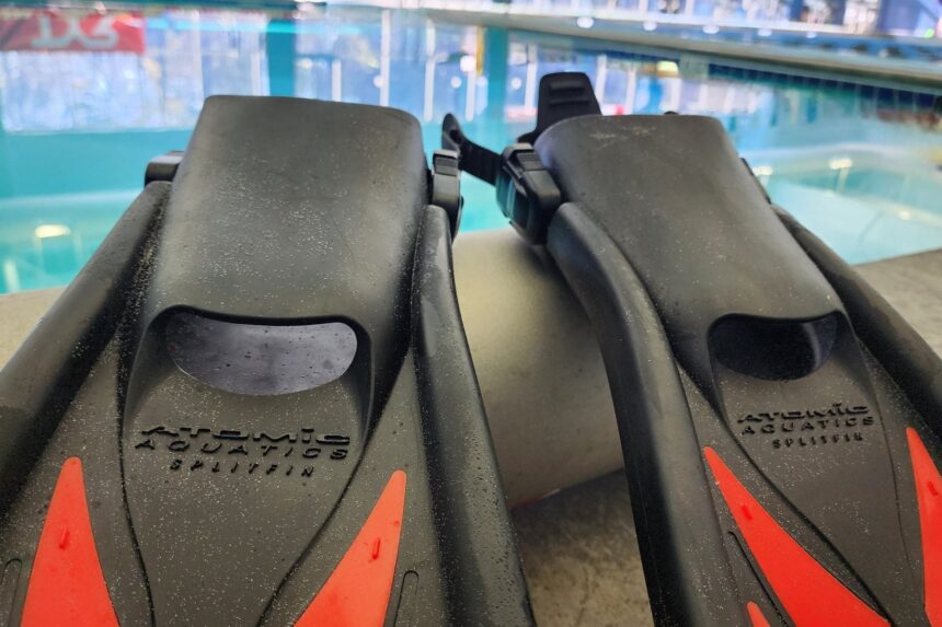 Atomic Aquatics SplitFin branding embossed on the foot pockets of two fins beside a pool
