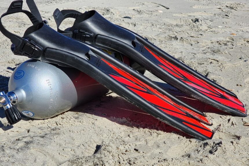Atomic Aquatics SplitFins leaning against a scuba cylinder half buried in beach sand