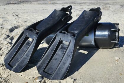 Black ScubaPro S-Tek fins lying in the sand next to a scuba cylinder during beach testing