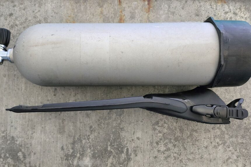 TUSA Solla fin laid beside an aluminum cylinder showing its slim side profile
