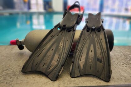 Black TUSA Solla fins resting on a pool deck with a scuba cylinder behind them