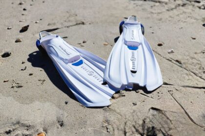 Pair of white and blue Aqua Lung Storm fins resting on wet sand at the water's edge