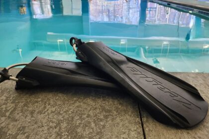 Two black Zeagle Recon paddle fins lying on a pool deck beside turquoise pool water
