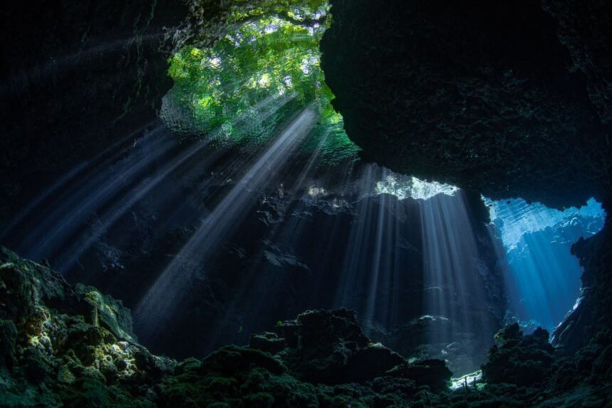 Sunbeams streaming through a cavern opening into the water below