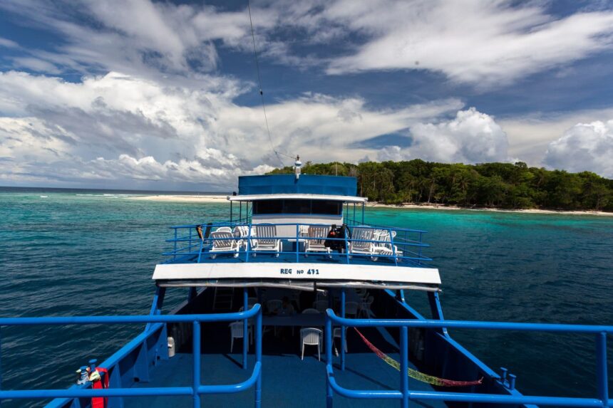 View from the Bilikiki's stern of a tropical island shoreline and reef flat