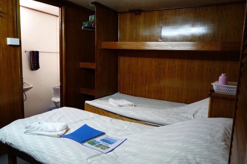 Twin beds made up with towels in a wood paneled cabin on the Bilikiki