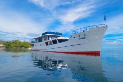 Bilikiki liveaboard boat anchored near a tropical shoreline with its reflection in calm water