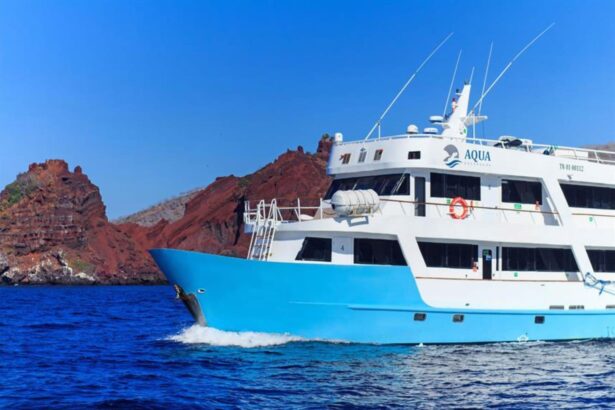 Aqua liveaboard cruising past red rock cliffs in the Galapagos