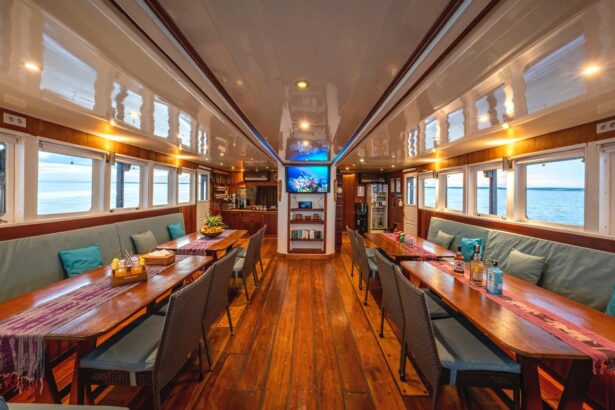 Dining saloon aboard the Ambai with long tables, a TV, and window views of the sea