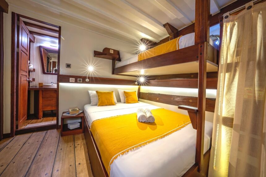 Wood-paneled cabin aboard the Ambai with a framed photo and bedside reading light