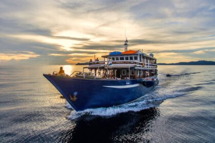 The Ambai liveaboard cruising into a golden sunset with its wake trailing behind