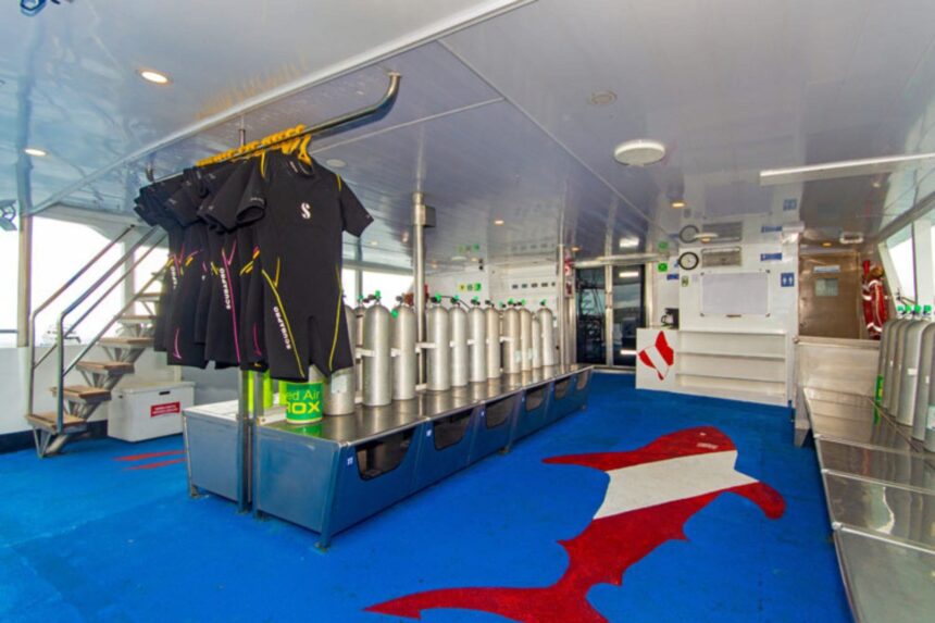 wetsuits hang above a row of scuba tanks on the Calipso dive deck