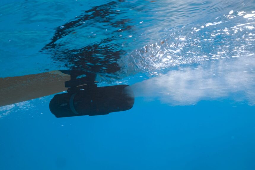 LEFEET P1 clamped under a paddleboard just below the surface, pushing a wake of bubbles