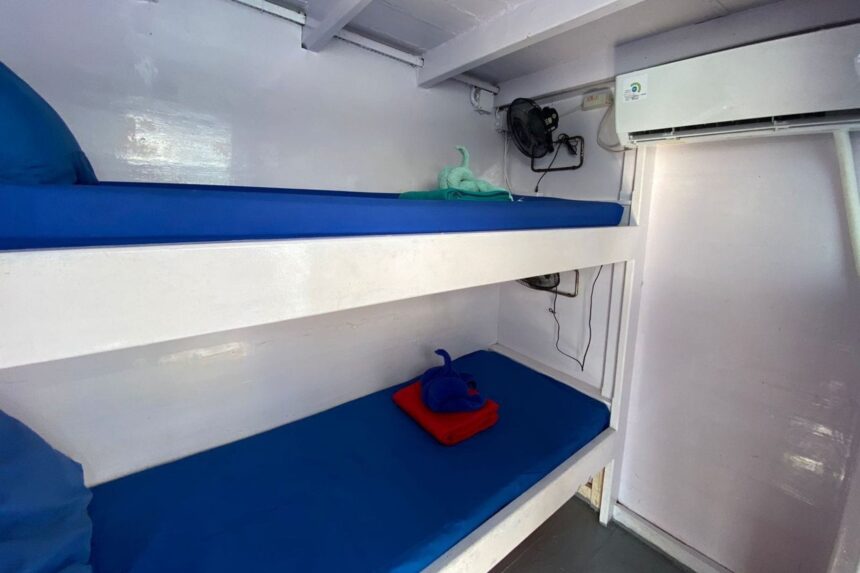 a simple bunk cabin aboard the Epica with two blue-cushioned beds