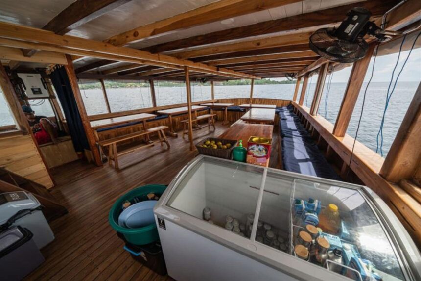 Covered dining and lounge deck of the Jaya with tables, benches and a drinks fridge