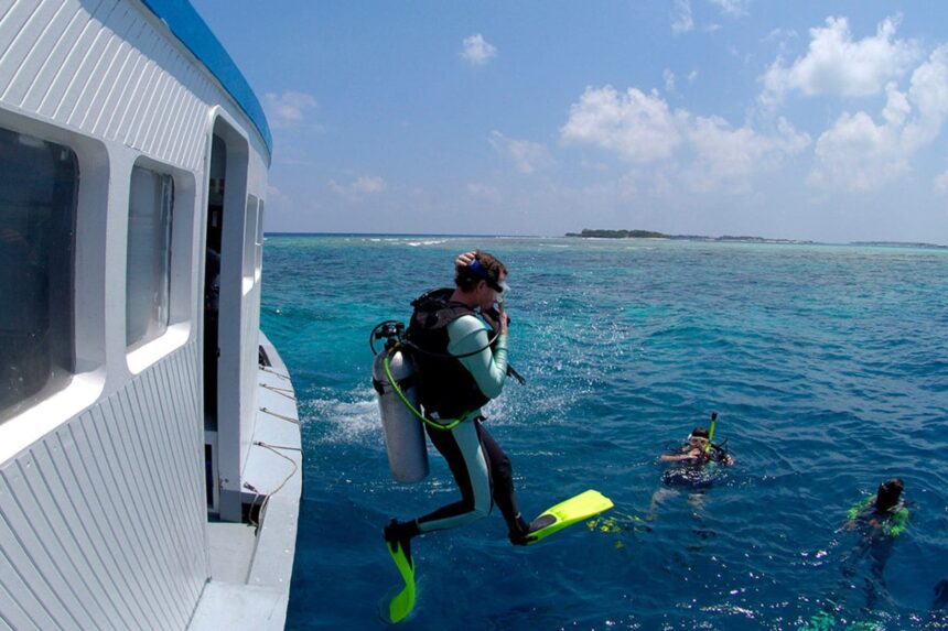 Diver in scuba gear jumping off the Manthiri's dive boat into turquoise water