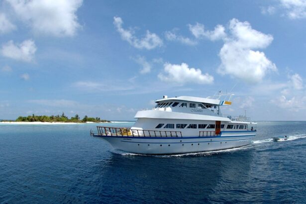 The Manthiri liveaboard cruising past a low sandy island with a trailing wake
