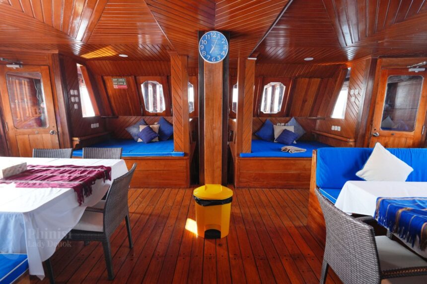 wood paneled lounge with dining tables and blue seating aboard Lady Denok