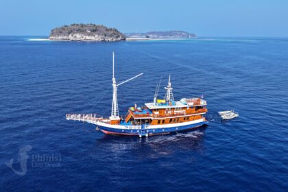 The Lady Denok phinisi liveaboard anchored near a small island under blue sky