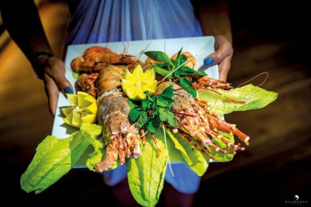 Server holding a plate of grilled lobster and prawns garnished with lemon