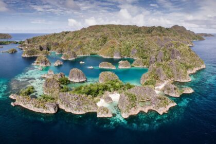 Aerial view of Raja Ampat's jagged limestone islets ringed by turquoise lagoons and shallow reef