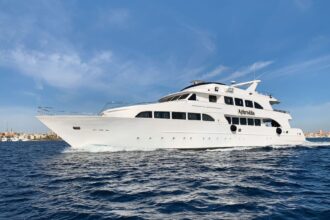 Aphrodite liveaboard yacht cruising past a coastal town on blue water