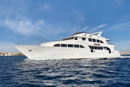 Aphrodite liveaboard yacht cruising past a coastal town on blue water