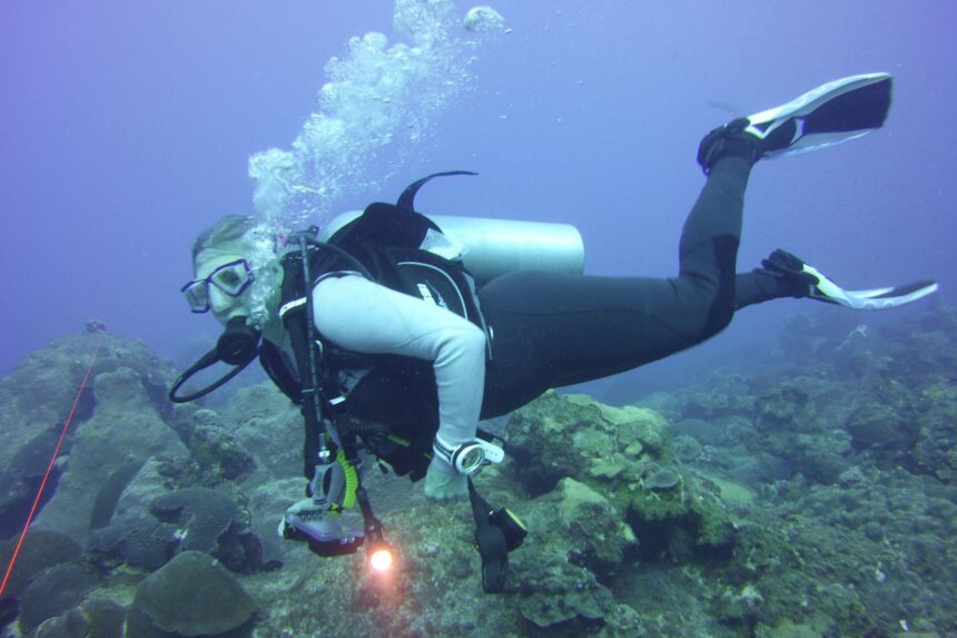 Our tester diving in the Aqualung XSCAPE wetsuit over a reef with a dive light in hand