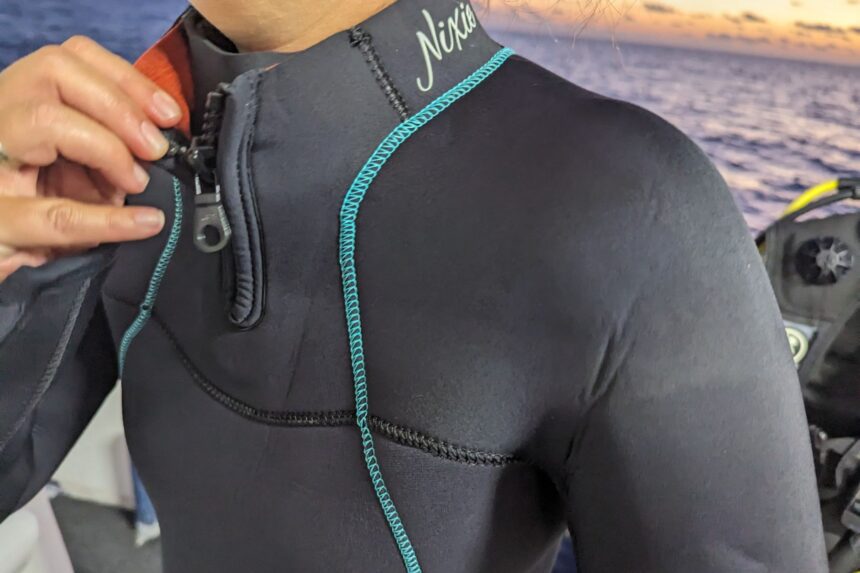 Hand pulling the neck zip on the BARE Nixie Ultra, with the Nixie logo on the shoulder