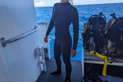 Our reviewer on a dive boat in the smooth navy Fourth Element Surface wetsuit, scuba gear racked behind