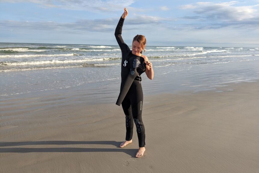 Our tester raising one arm in the ScubaPro Everflex Yulex wetsuit to test shoulder mobility on the beach