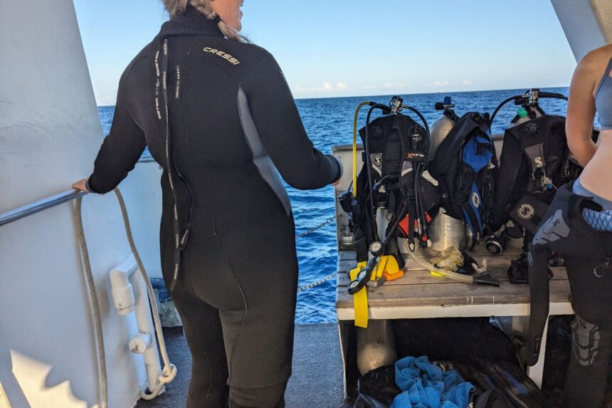Cressi Otterflex Back On The Boat Back view of our tester in the Cressi Otterflex wetsuit on a dive boat, with rigged BCDs behind