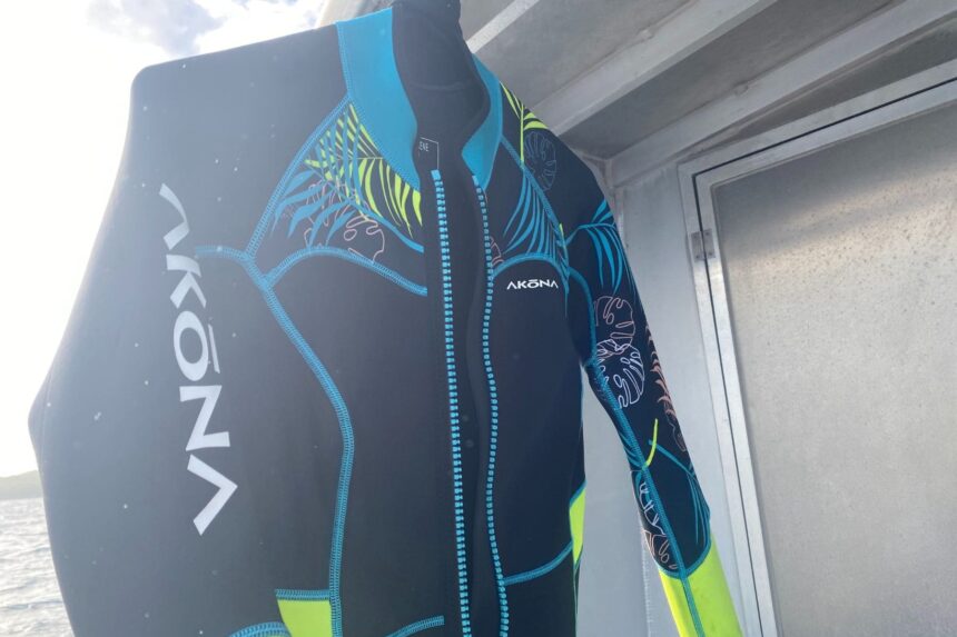 Akona Tropic wetsuit hanging on a boat, showing its front zip and tropical foliage print