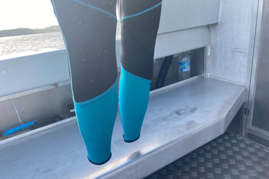 Lower legs of the Akona Tropic wetsuit with turquoise calf panels, on a dive boat bench