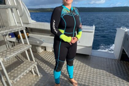 DIVEIN tester wearing the black Akona Tropic wetsuit with blue and lime trim on a boat deck