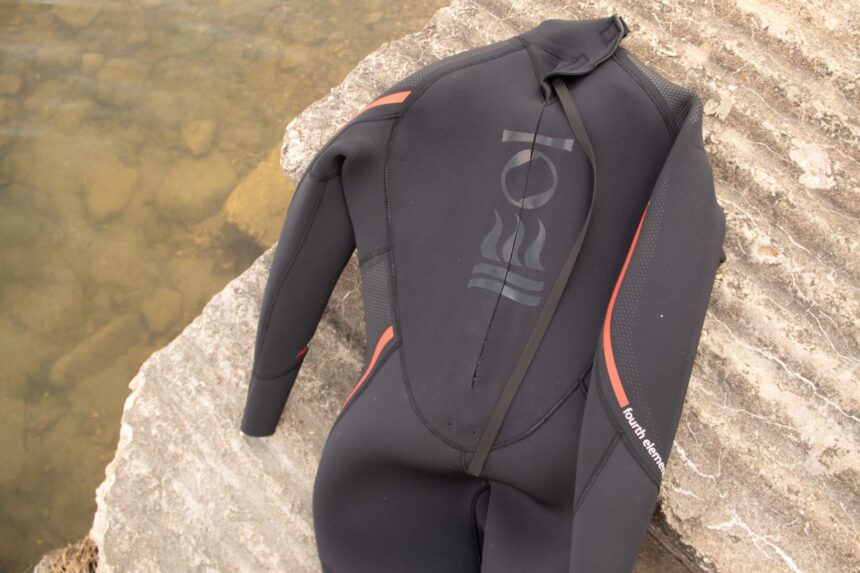 Fourth Element Proteus II wetsuit laid on rock showing the back panel, logo and long zip pull