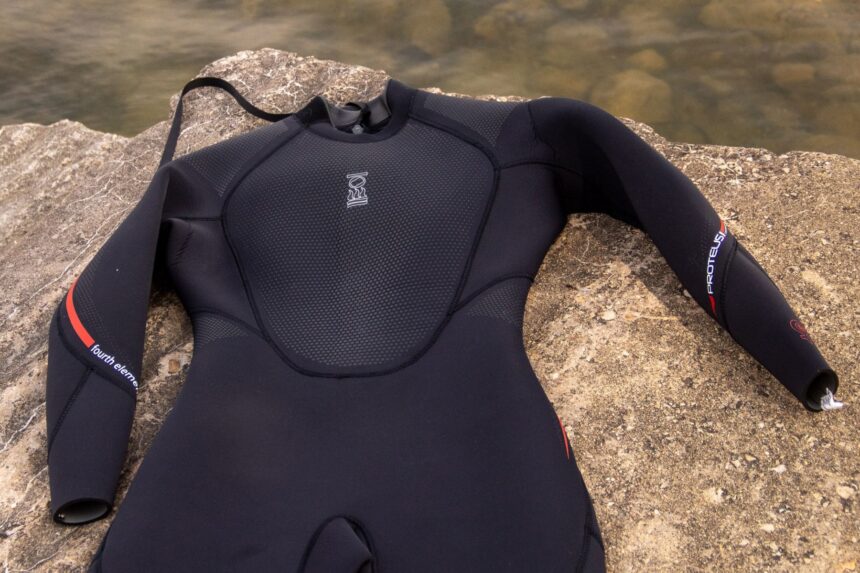 Fourth Element Proteus II wetsuit laid flat on rock by the water, showing the textured chest panel