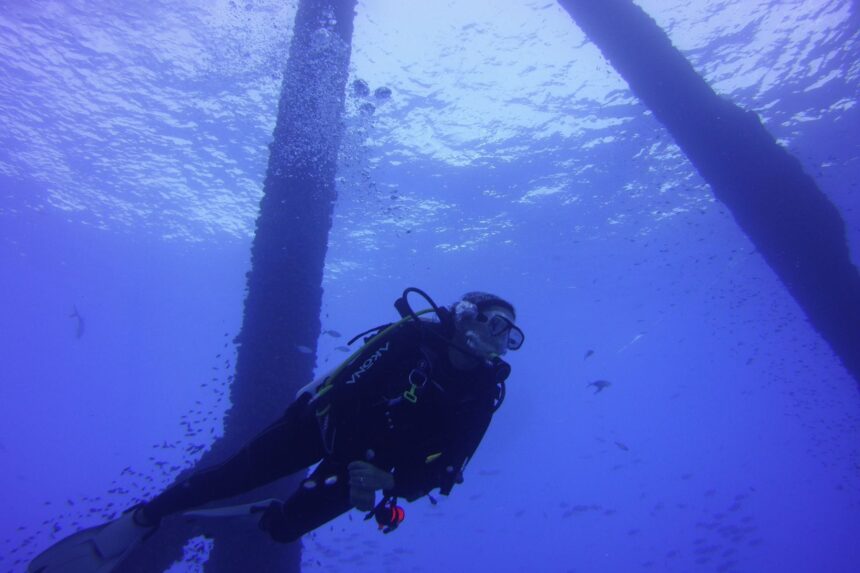 Our tester diving in the Akona Back Zip Classic wetsuit beneath a boat with sunlight overhead