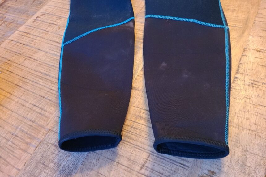 Both ankle cuffs of the Akona Back Zip Classic wetsuit laid on a wooden floor with blue stitching