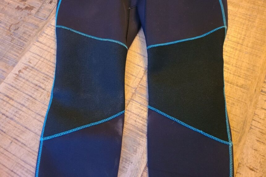 Legs of the Akona Back Zip Classic wetsuit laid on a wooden floor showing blue stitched panels