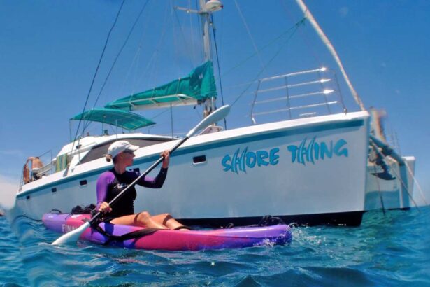 A woman paddling a kayak beside the Shore Thing catamaran