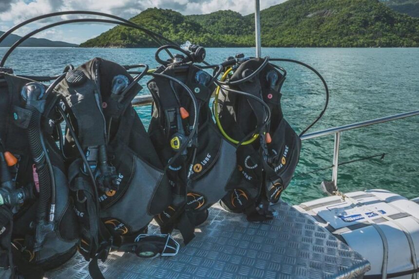 Scuba tanks and BCDs racked on deck with green hills in the background
