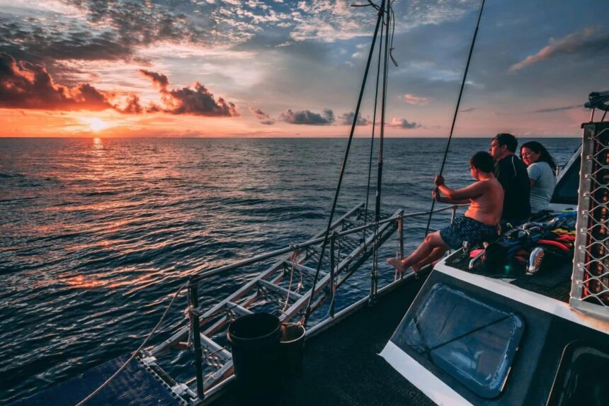A family watching the sunset from the deck of a liveaboard at sea