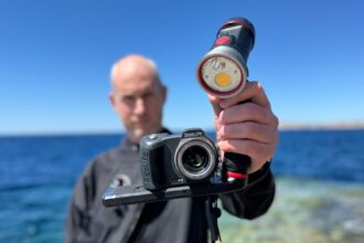 Our reviewer holding up the SeaLife Micro 3.0 camera and a video light on a tray by the sea